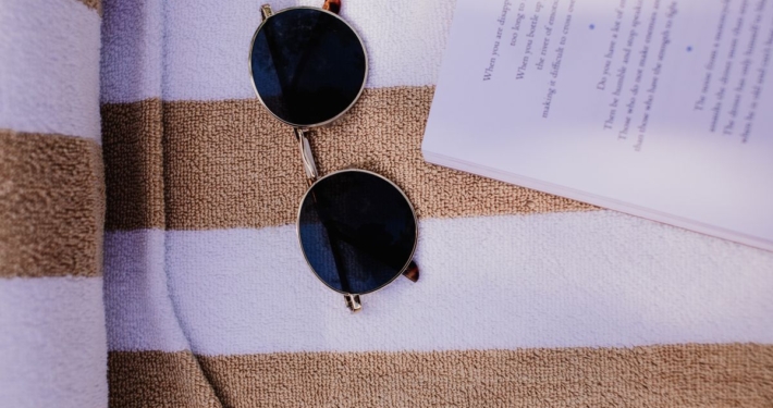 Open boek en zonnebril op een strandhanddoek, vakantiethrillers van Suzanne Vermeer